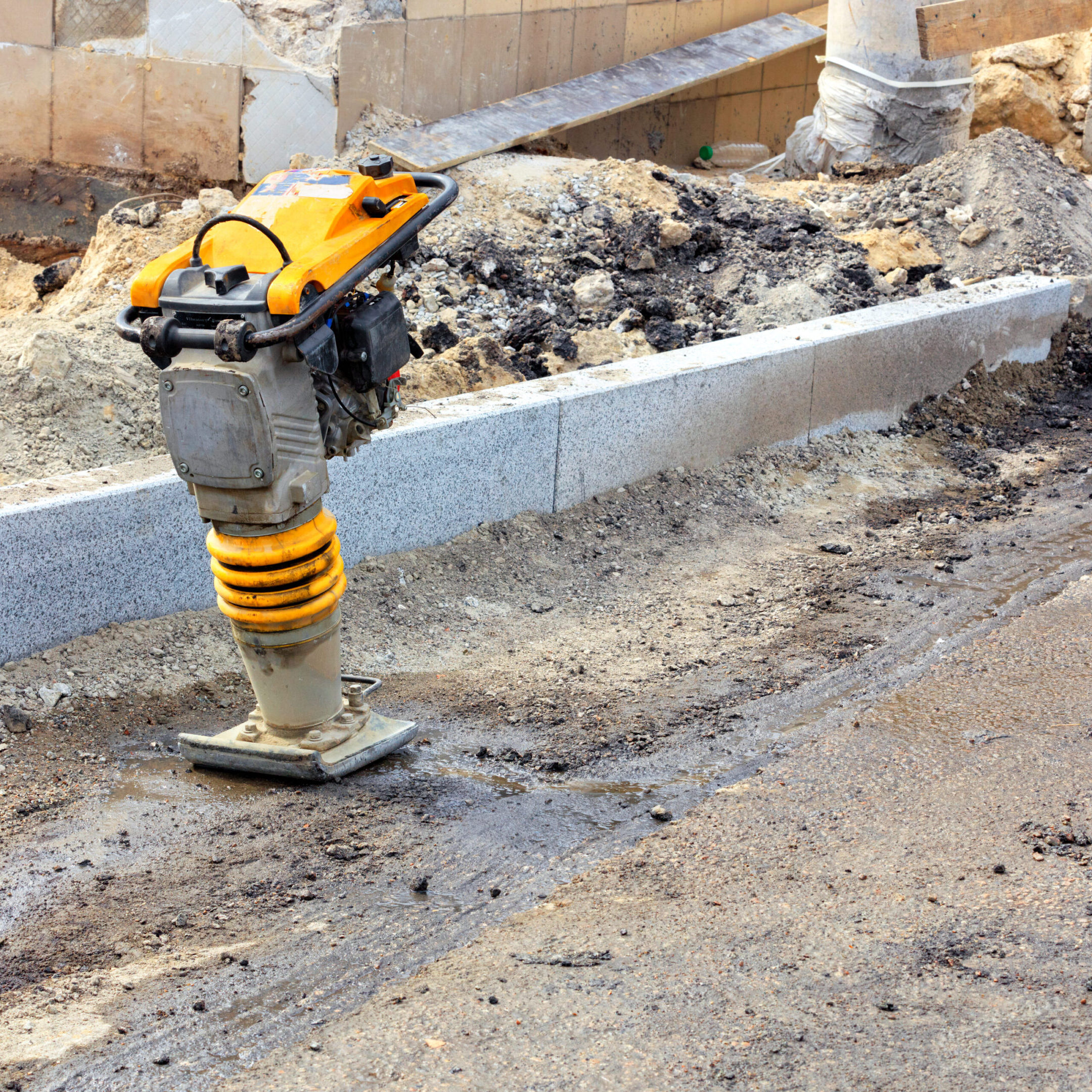 Petrol vibro rammer is used on a hard-to-reach working place in the background of a road construction site.