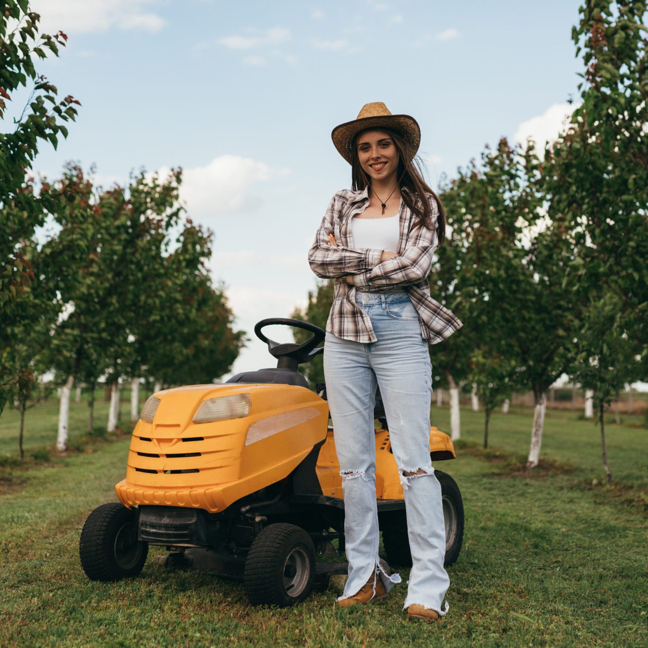 woman posing beside lawn mower in orchard